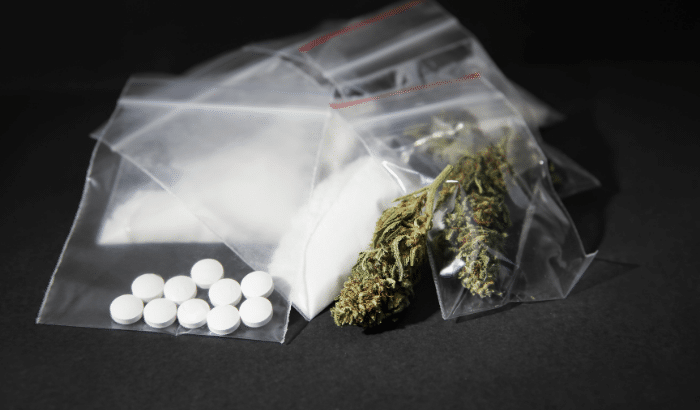 Drugs like marijuana, cocaine, and other unknown pills are shown in small bags for distribution. 